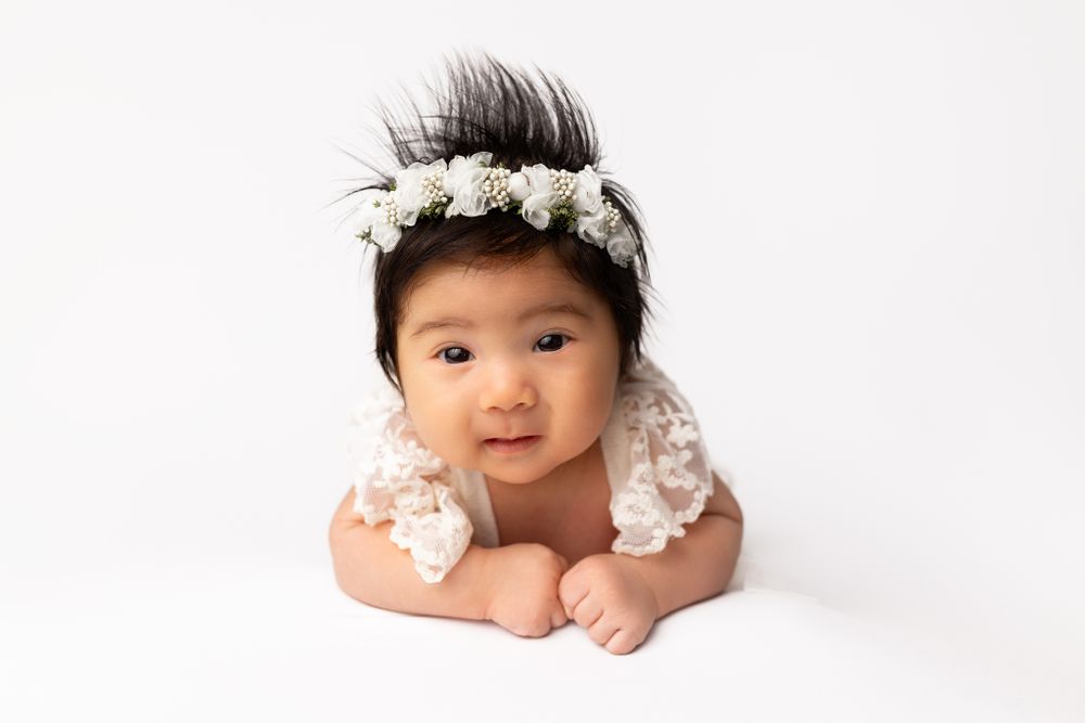 Baby wearing floral headband lying on white background.
