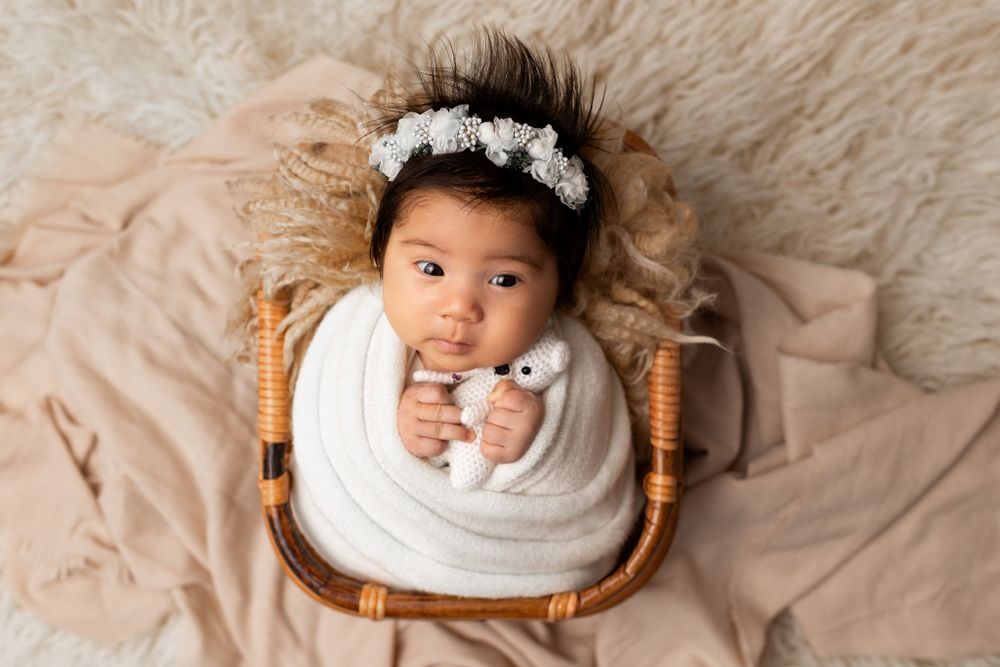 Baby swaddled in white wrap lying in wooden chair on beige background.
