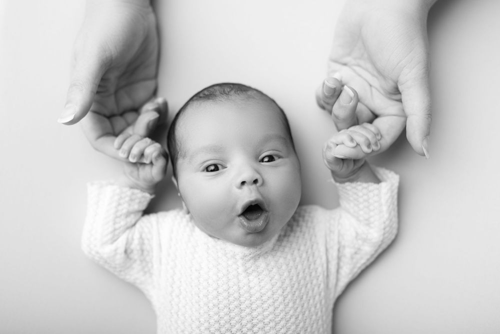 Baby in white sweater making expression while lying on back.