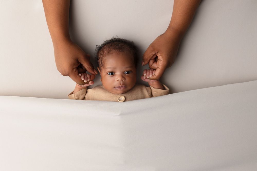 Creative newborn portrait with hands framing baby against white background.