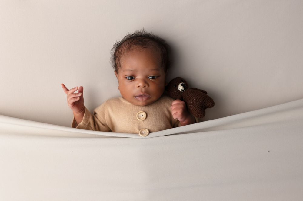 Baby wearing beige outfit lying on light colored background.