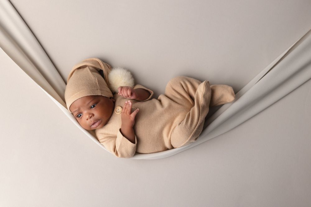 Peaceful sleeping newborn in beige outfit resting in fabric hammock during photo session.