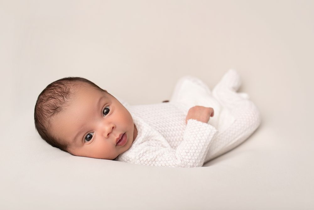 Baby in white knit outfit lying on neutral background.