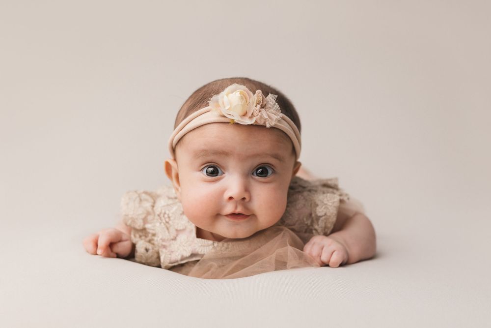Baby wearing headband lying on beige blanket.