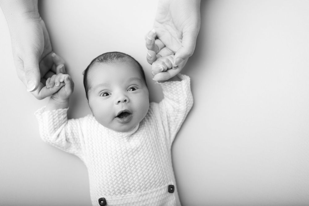 Black and white portrait of a small baby in white clothing making an excited expression.