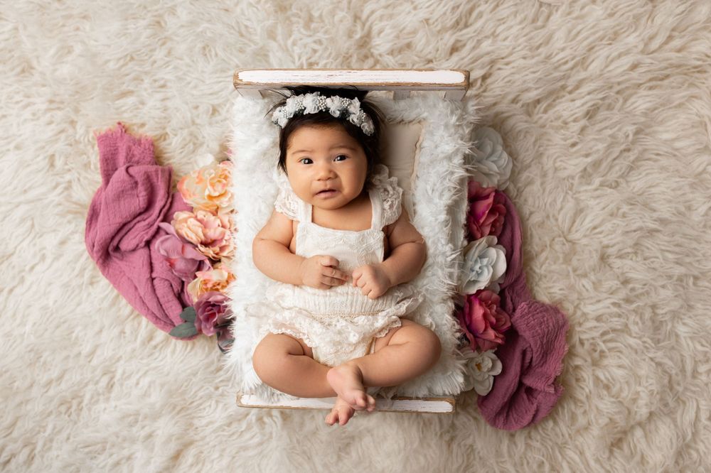 Baby in white outfit lying in basket with pink fabric decorations.