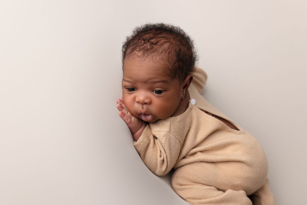 Sleepy newborn in beige outfit lying on light background during photo session.