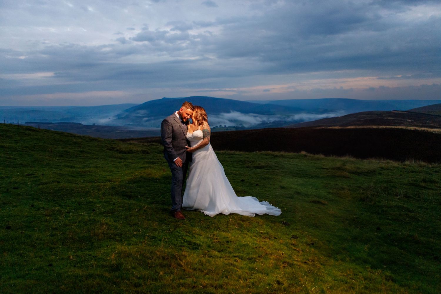 Romantic sunset portrait of couple embracing on hilltop with mountain landscape.