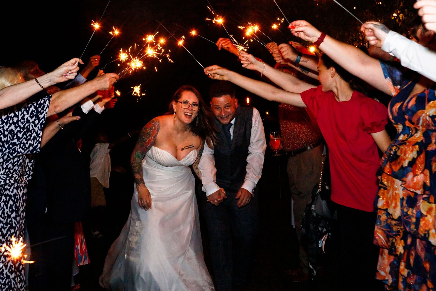 Wedding celebration with sparklers creating magical light tunnel effect at night.