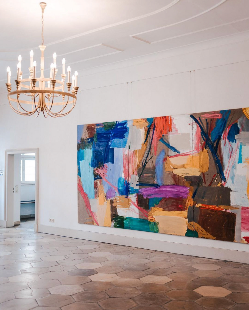 Modern art gallery space with colorful abstract paintings and elegant chandeliers.