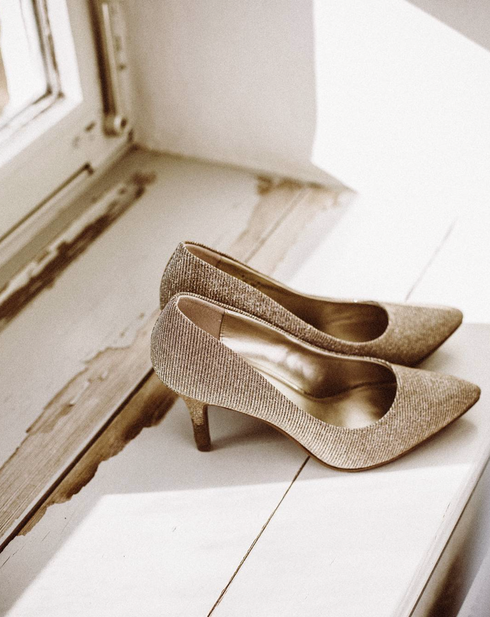 Elegant sparkly gold high heel shoe displayed on white wooden floorboards.