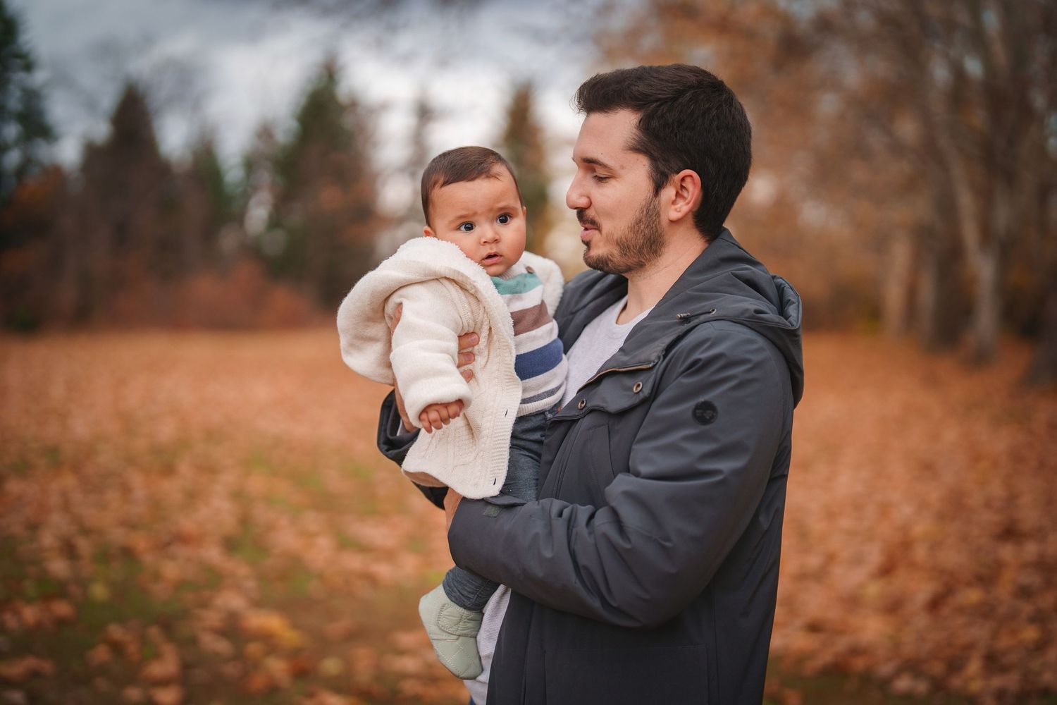 A tender moment between parent and baby against an autumn forest backdrop.