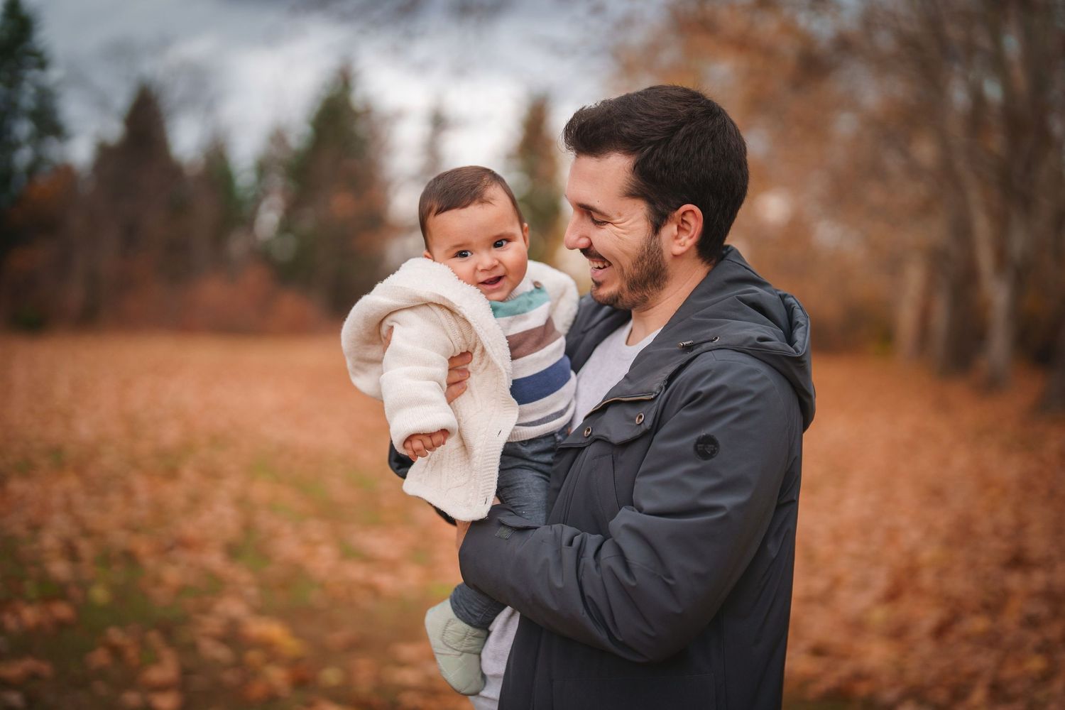 Parent holding and smiling at baby against autumn forest background.