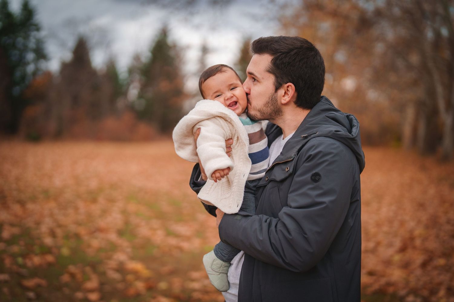 Parent sharing a sweet moment with baby outdoors during fall season.