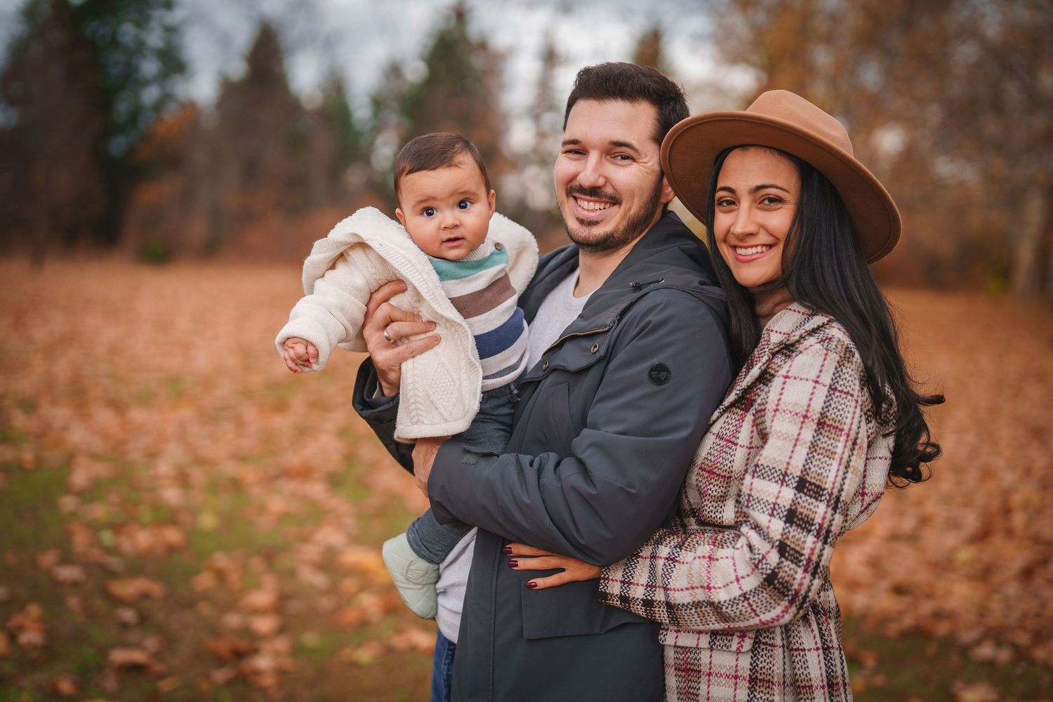 A family poses together on fallen leaves during an autumn photo shoot.