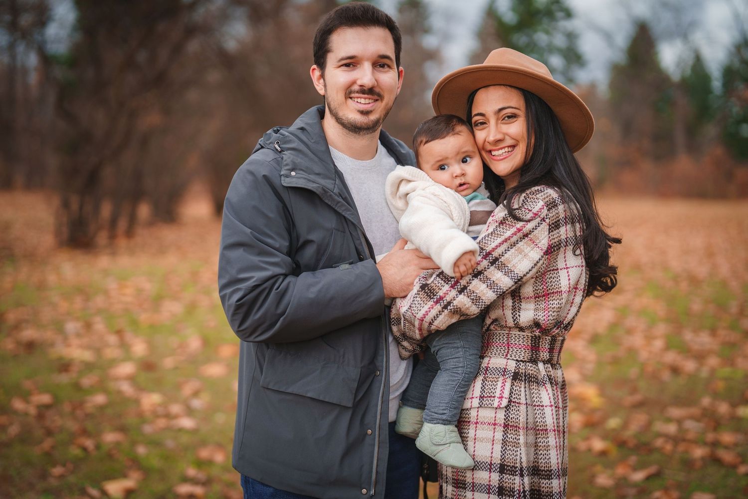 A family poses together in warm clothing during an autumn photo session.