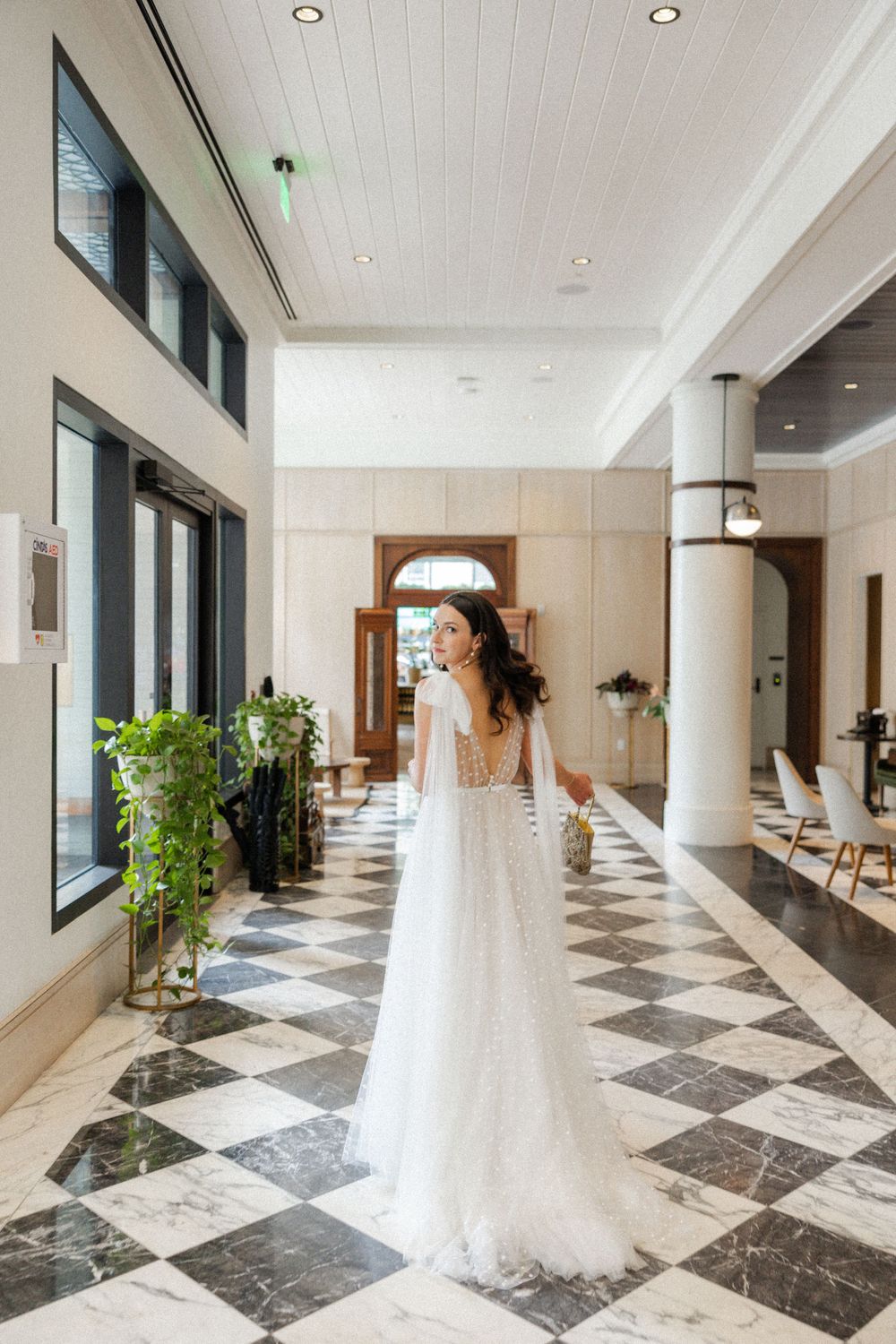 Wedding gown displayed in modern hallway with marble floors and white columns.