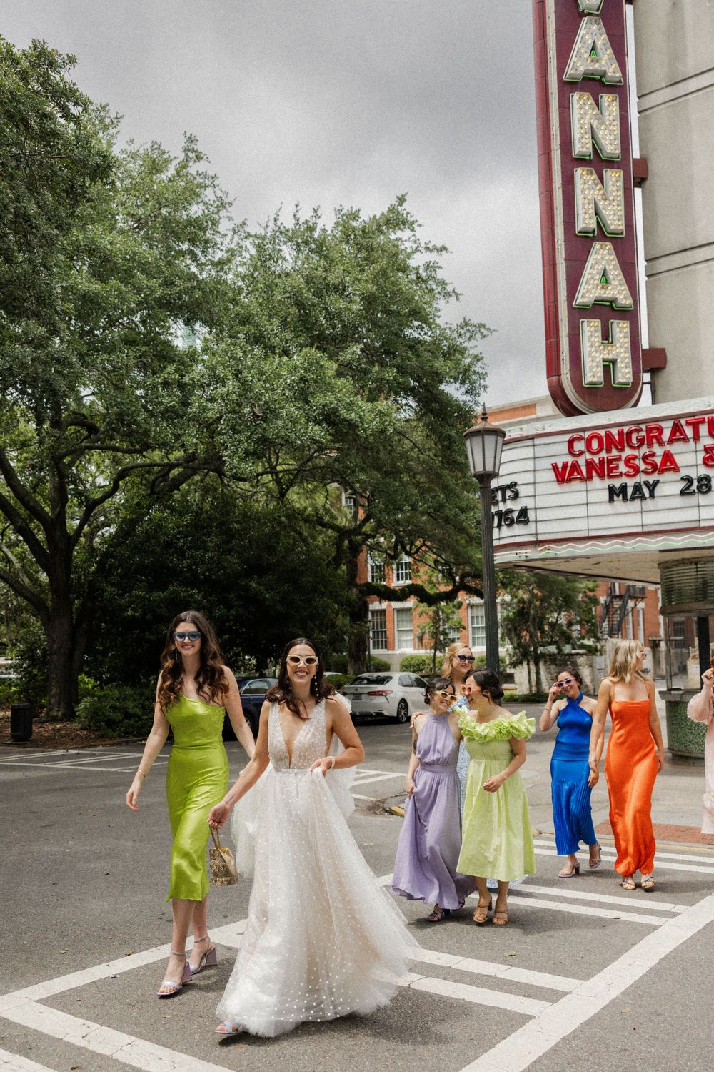 Bridal party in colorful dresses walking outside historic theater with marquee sign.