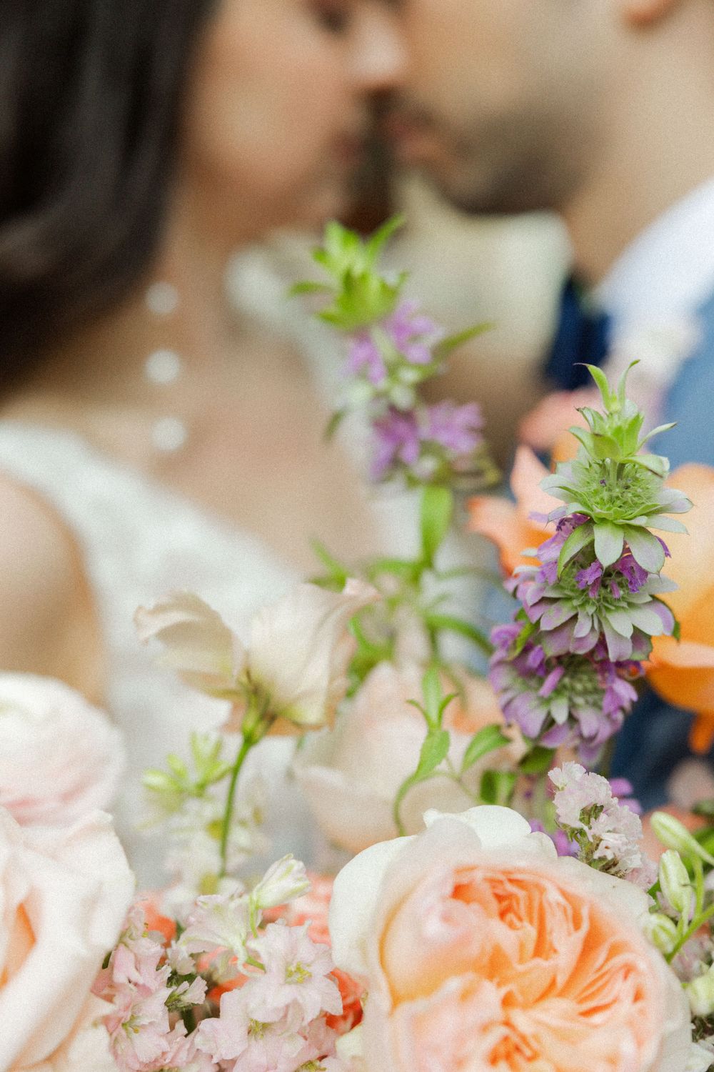 Delicate floral arrangement with peach roses and purple wildflowers in soft focus.
