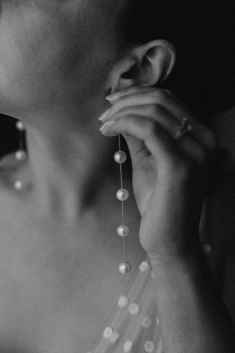 Pearl necklace being held up against a dark background in an artistic black and white composition.