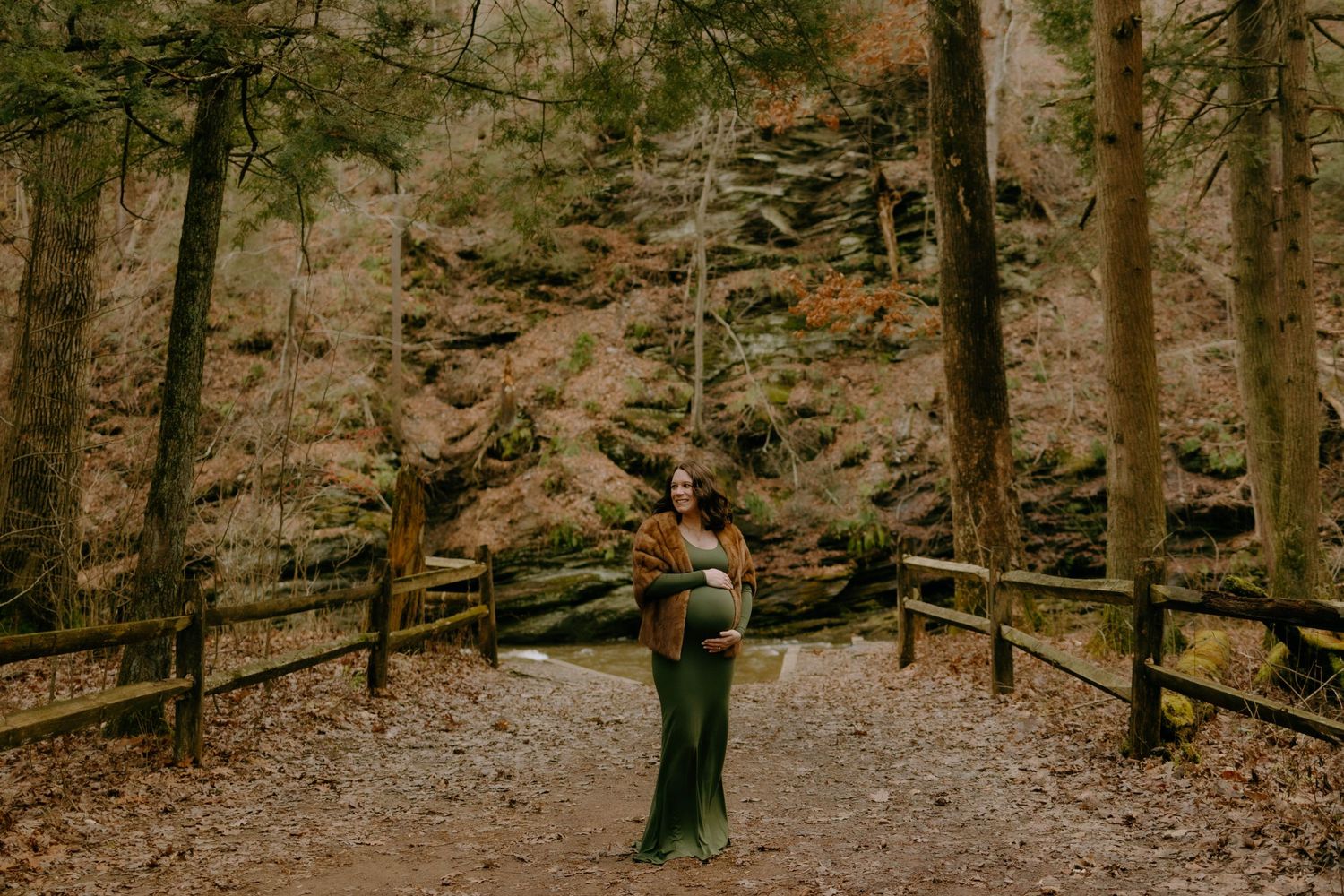 Person in outdoor winter attire standing on wooden walkway surrounded by bare autumn forest trees.