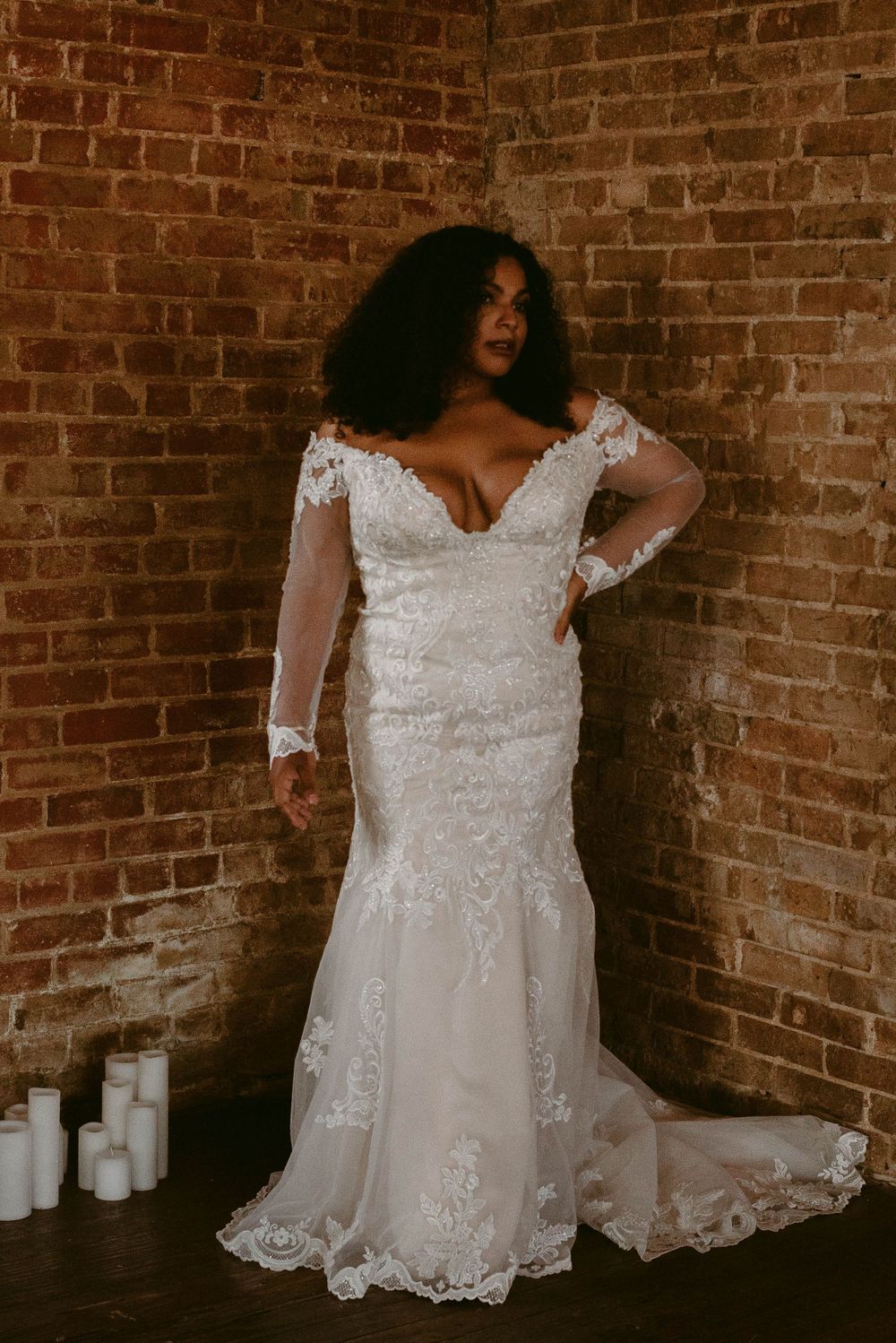 Elegant lace mermaid wedding gown with long sleeves against brick wall backdrop.