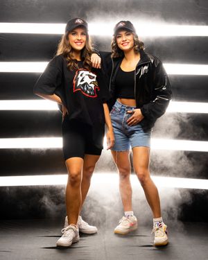 Two professional dancers in casual outfits posing together against a backdrop with horizontal illuminated stripes and dramatic fog effects.