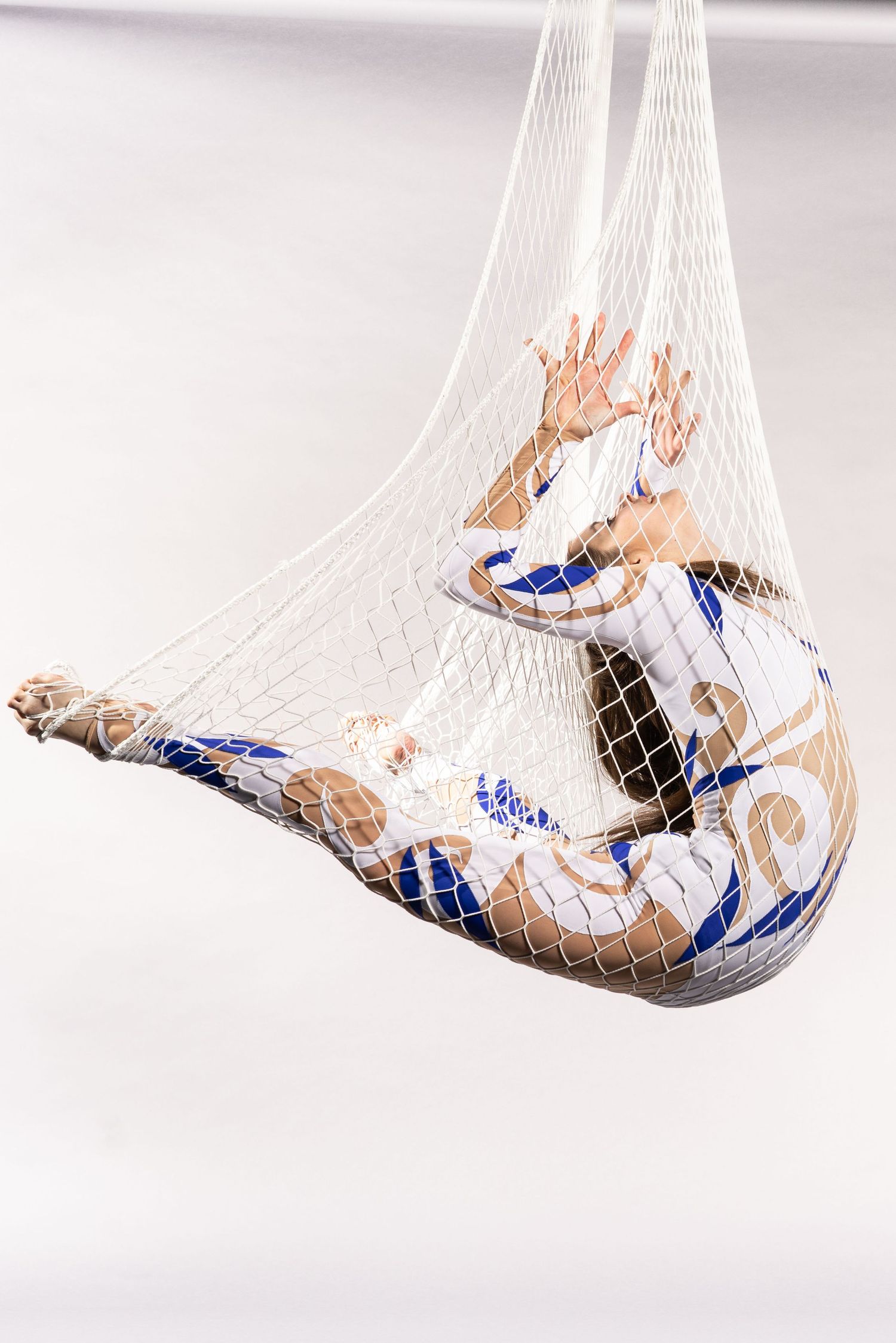 performance photography of circus performer hanging in a net wearing a blue and white leotard