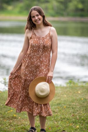 A summer portrait showing a floral dress and wide-brimmed hat by a lakeside setting.