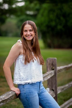 A casual summer portrait showing white top and jeans while leaning on a rustic wooden fence.