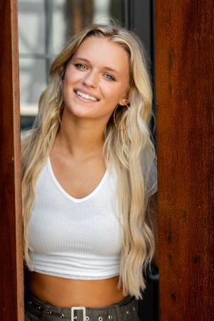 Portrait of person in white crop top framed by wooden doorway.