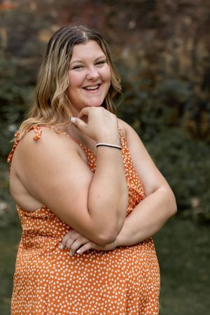 Portrait of person in orange polka dot dress posing against natural background.