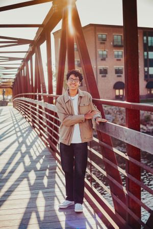 Stylish outdoor portrait on red bridge during golden hour with city buildings in background.