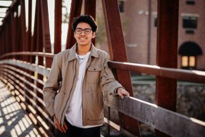 Casual portrait on rustic bridge with industrial architecture in background.