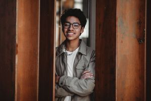 Casual portrait between wooden columns with natural lighting.