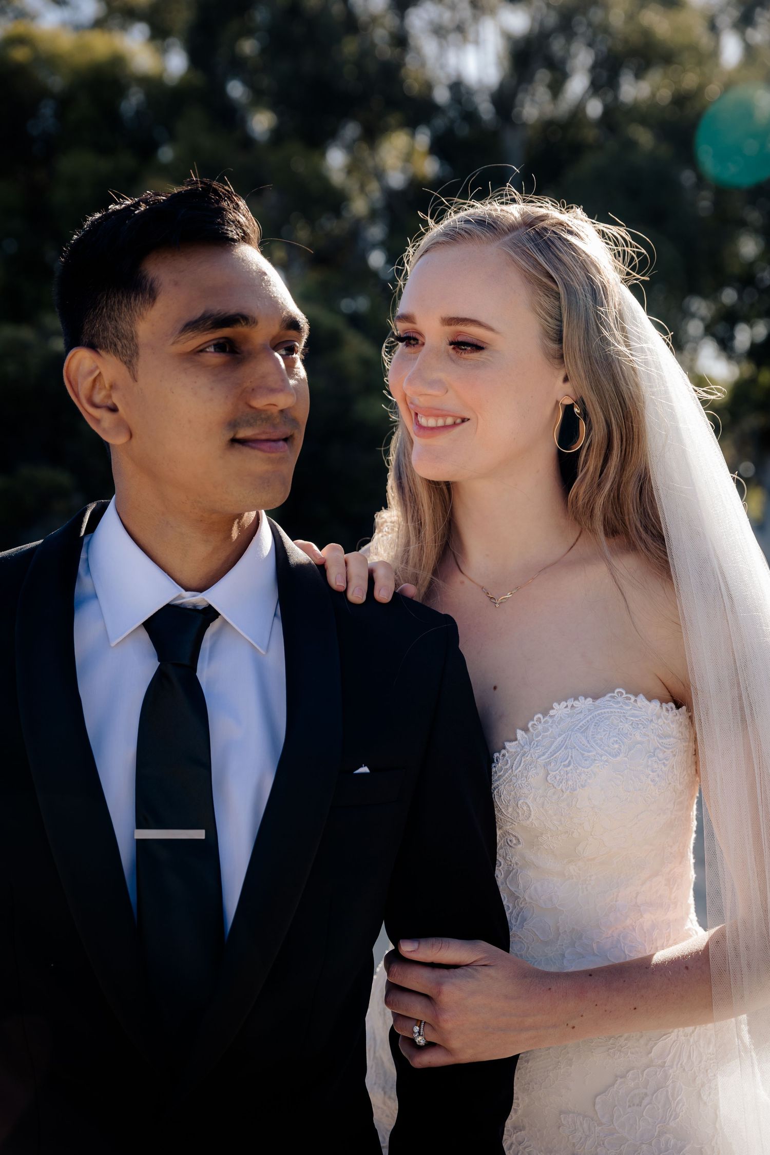 A couple in wedding attire share an affectionate moment outdoors in natural lighting.