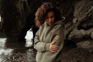 Figure in gray hoodie sitting on rocky coastline near ocean.