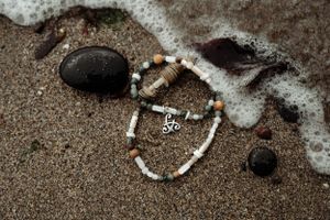 Shell and bead necklace lying on wet sand with ocean waves in background.