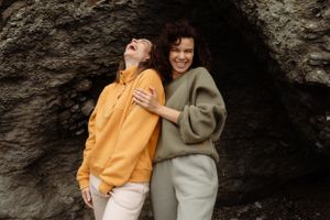 Group wearing yellow and neutral sweaters embrace joyfully against textured rock wall.