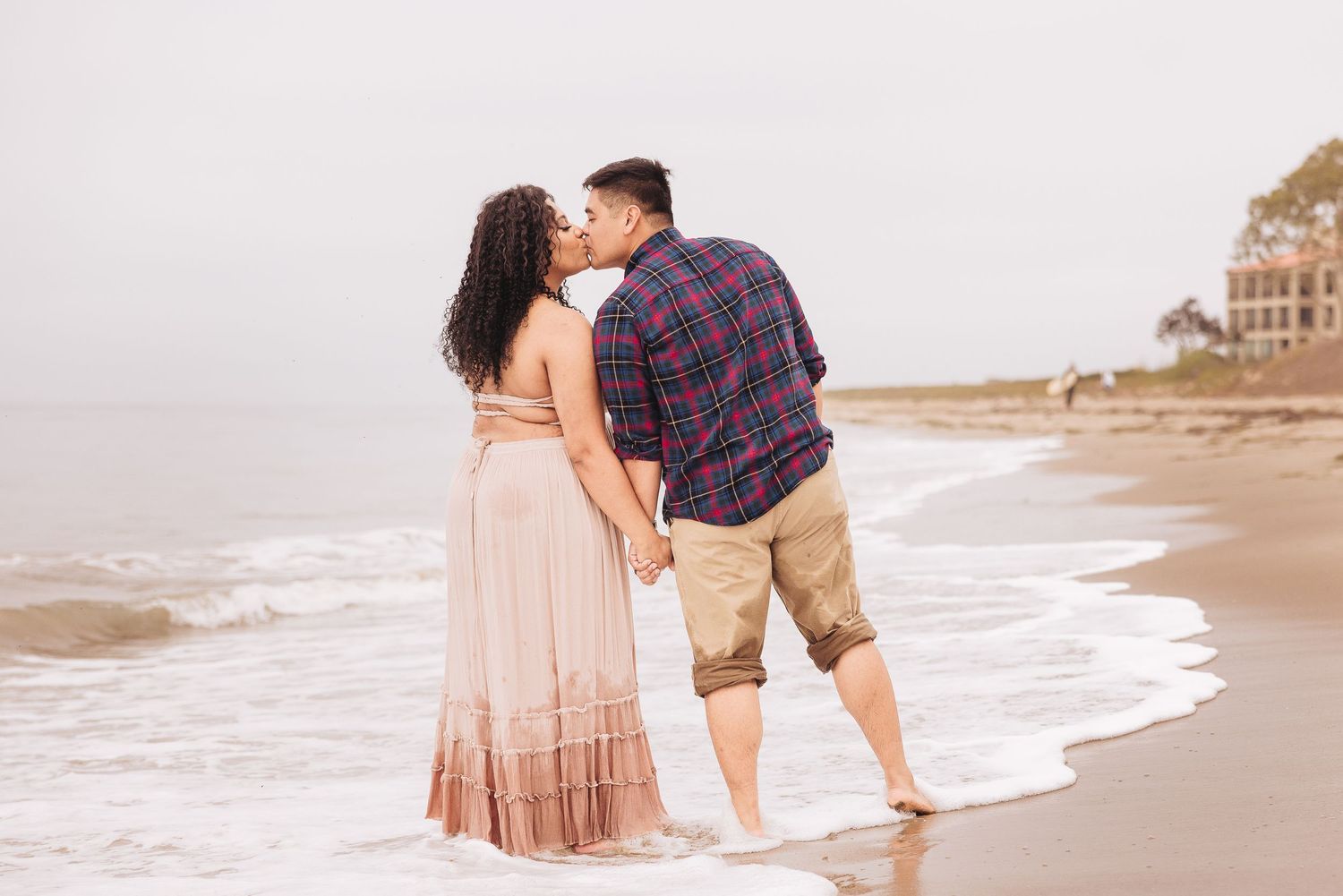 Romantic couple embracing while standing in ocean waves at sunset near coastal cliffs.