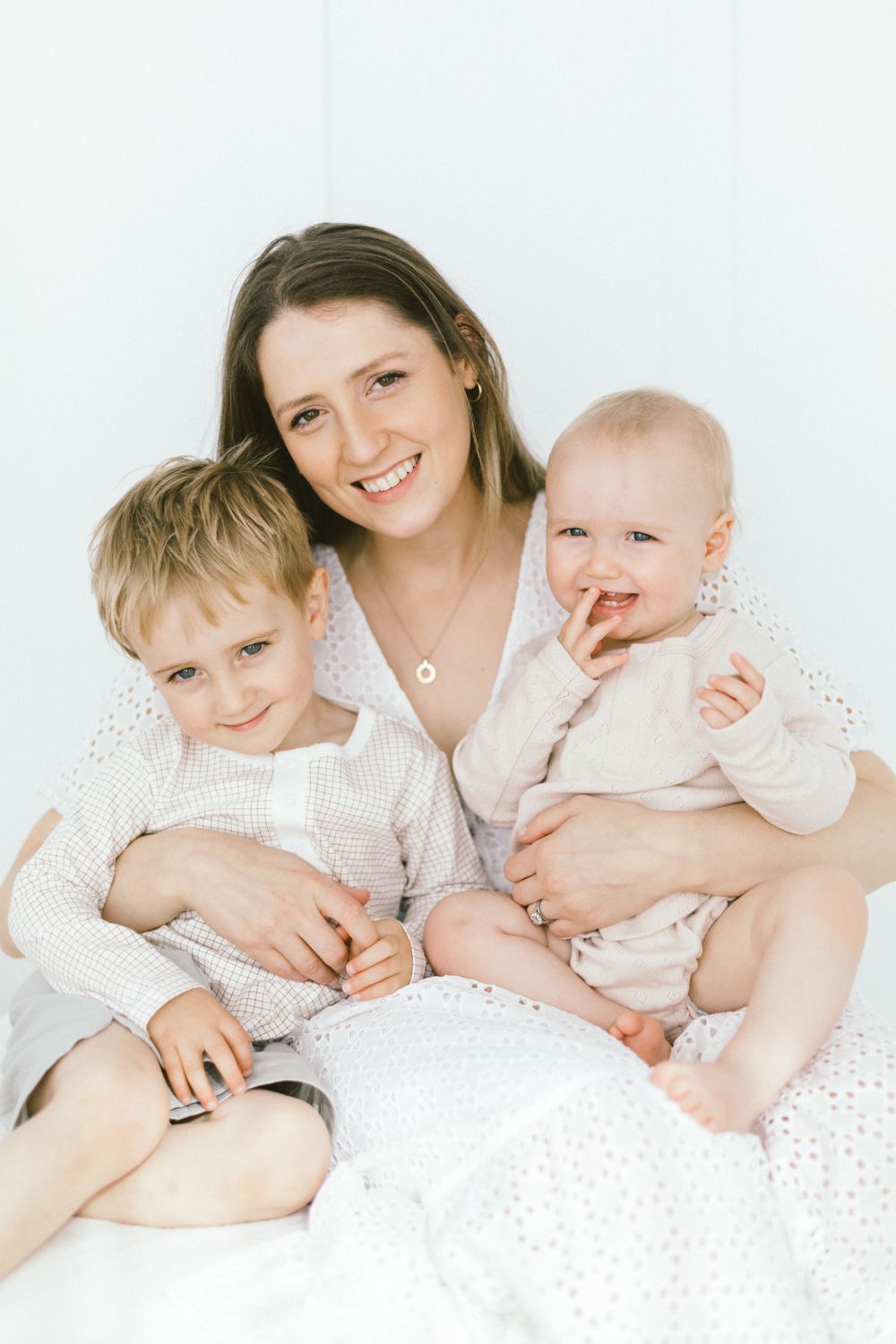Family relaxes together on white bedding in bright studio setting.