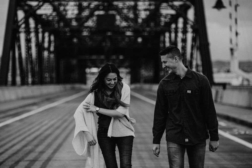 A couple walking and laughing together on a steel bridge structure.