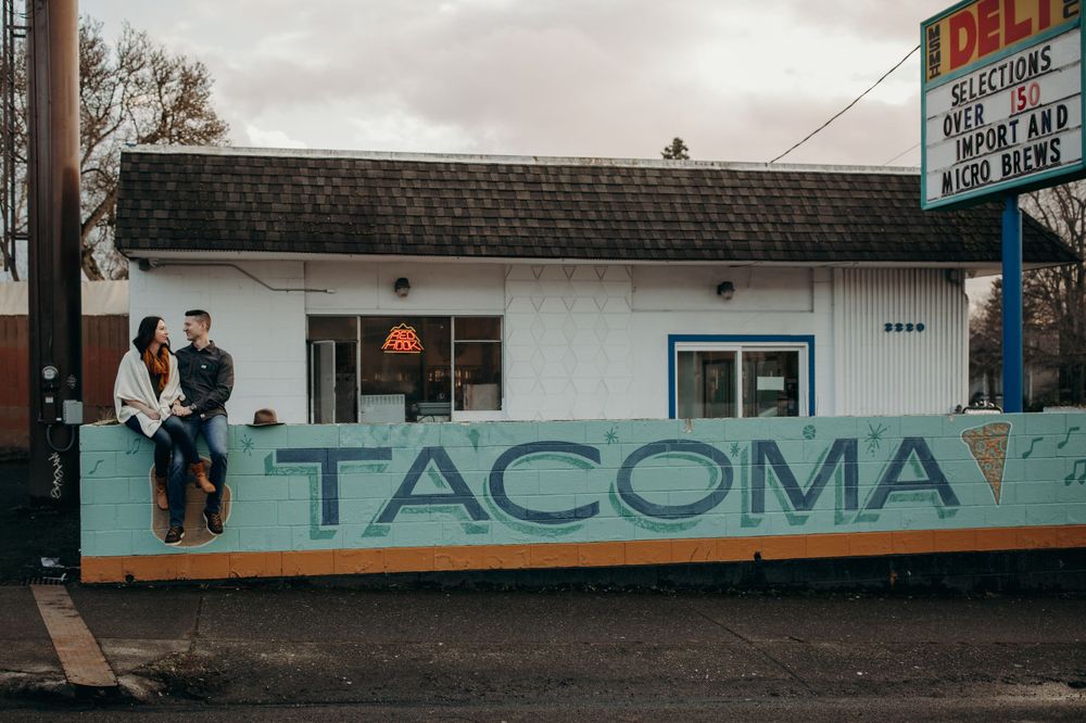 A couple sits on a retro-style building with Tacoma text painted on its facade.
