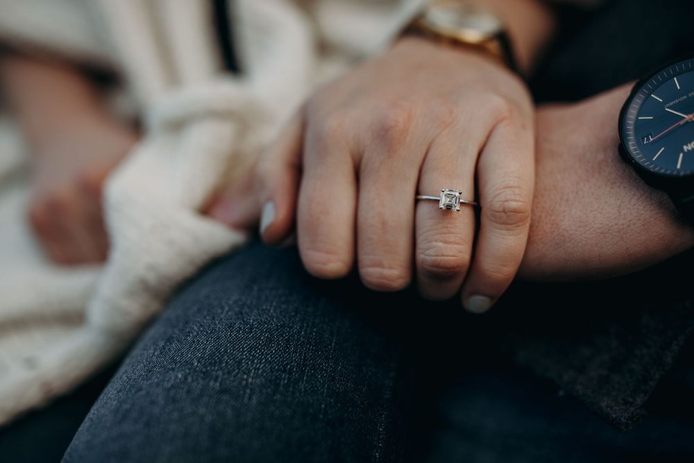 Close-up shot of a hand wearing a delicate engagement ring against denim jeans.