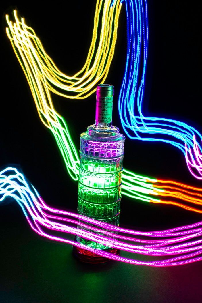 Decorative glass bottle illuminated by colorful neon light trails creating dynamic light painting effect.