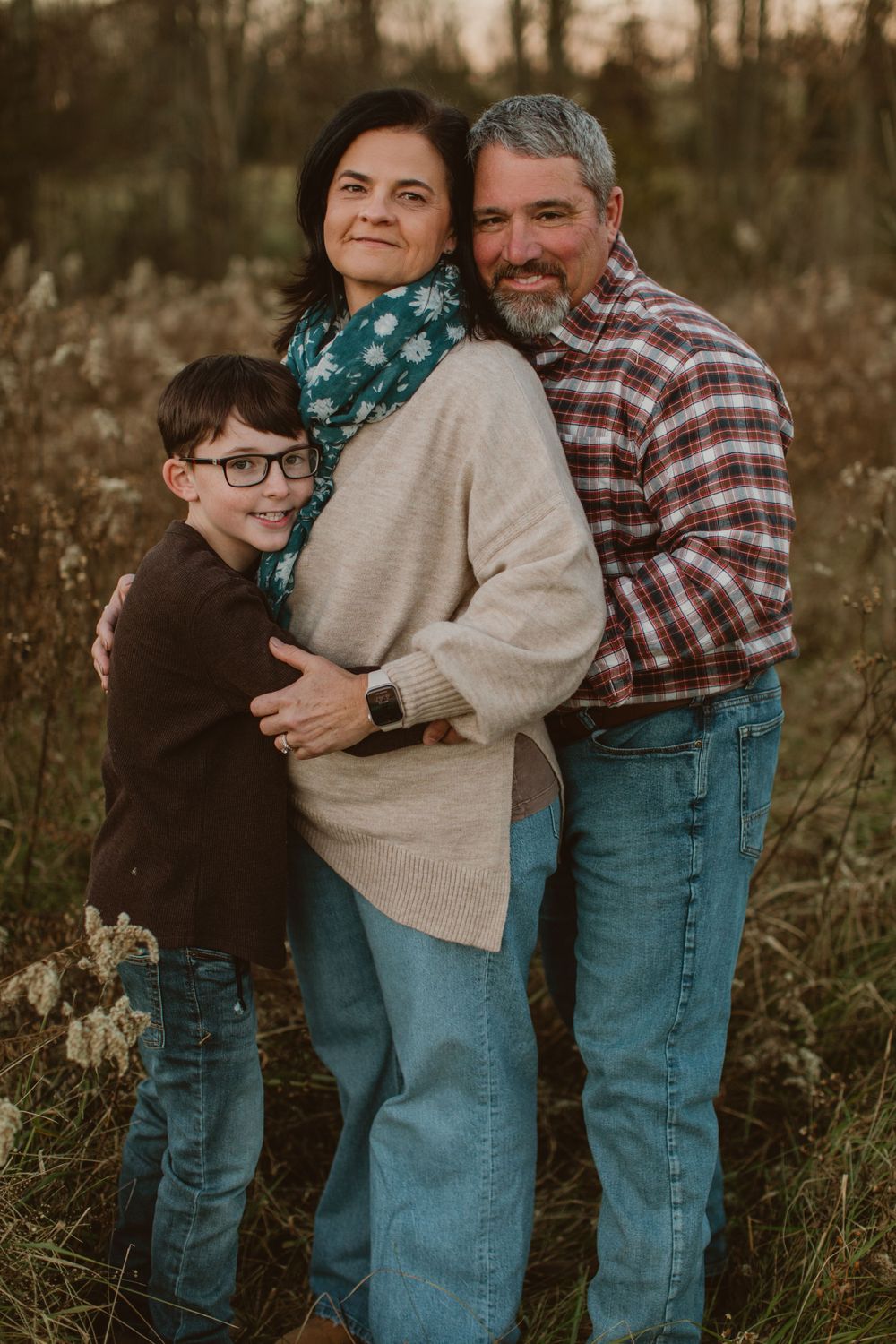 Family of three embracing outdoors during autumn sunset portrait session.