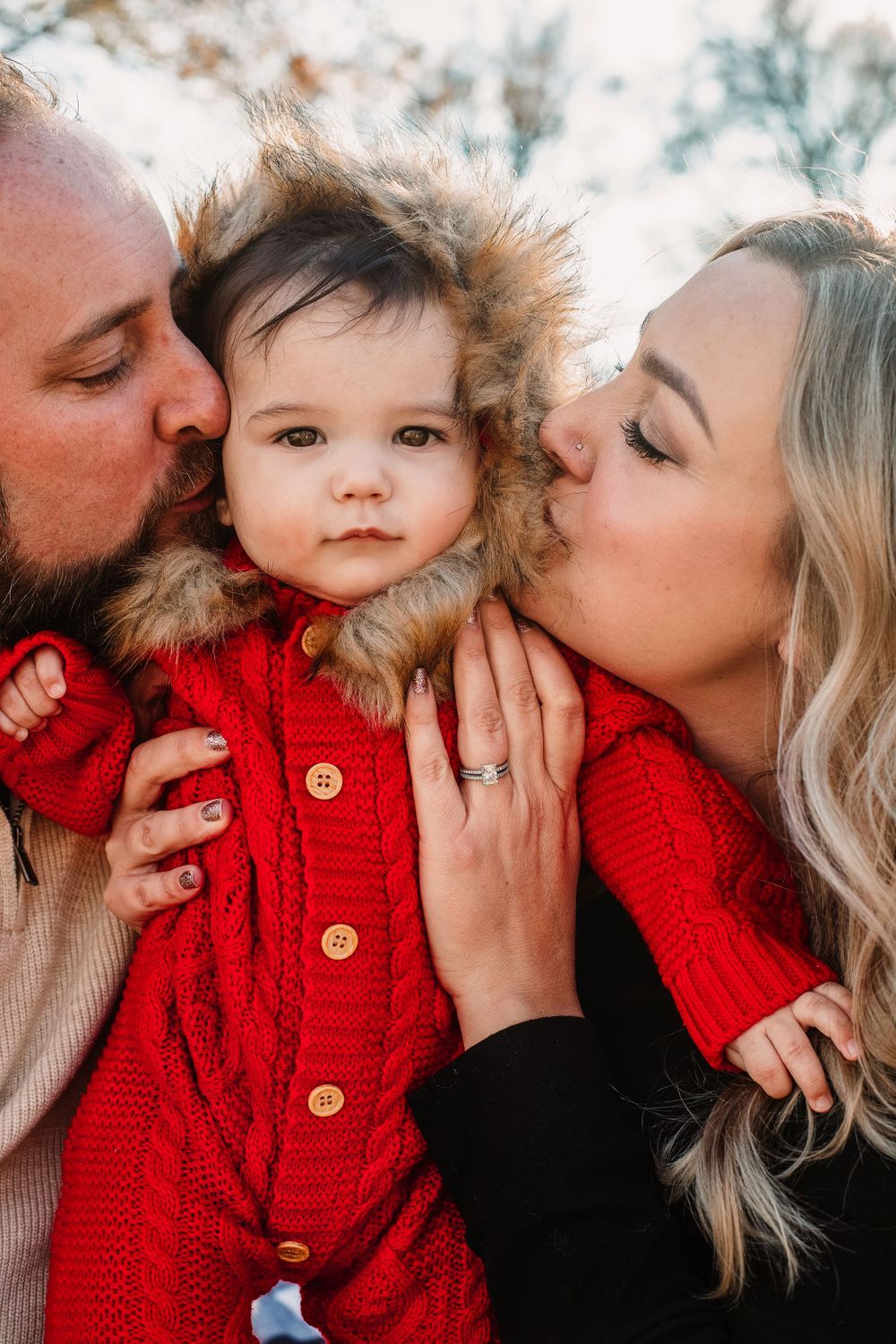Sweet family moment with child in red knit sweater receiving kisses.