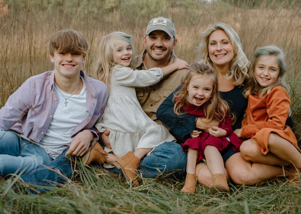 Family group lounging together in tall grass during golden hour.