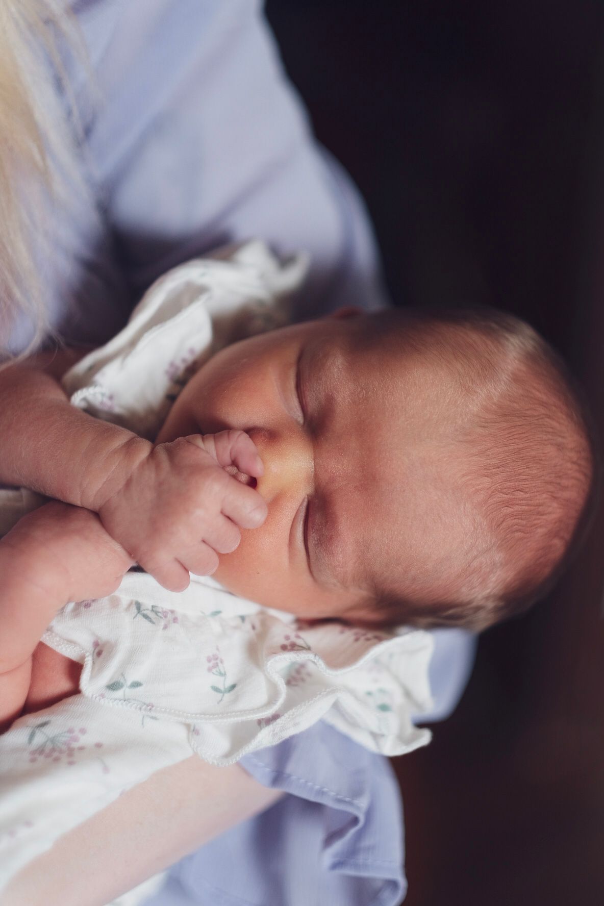 A mother wearing lavender holds her newborn baby girl who is clutching her hand against her face