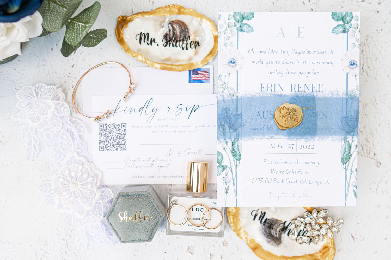 Wedding invitation suite with blue watercolor details, wax seal, and perfume on white lace background.